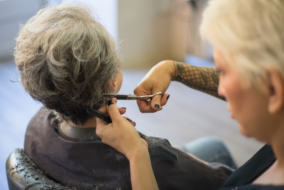 Hairdresser styling senior woman gray hair in salon for coverage
